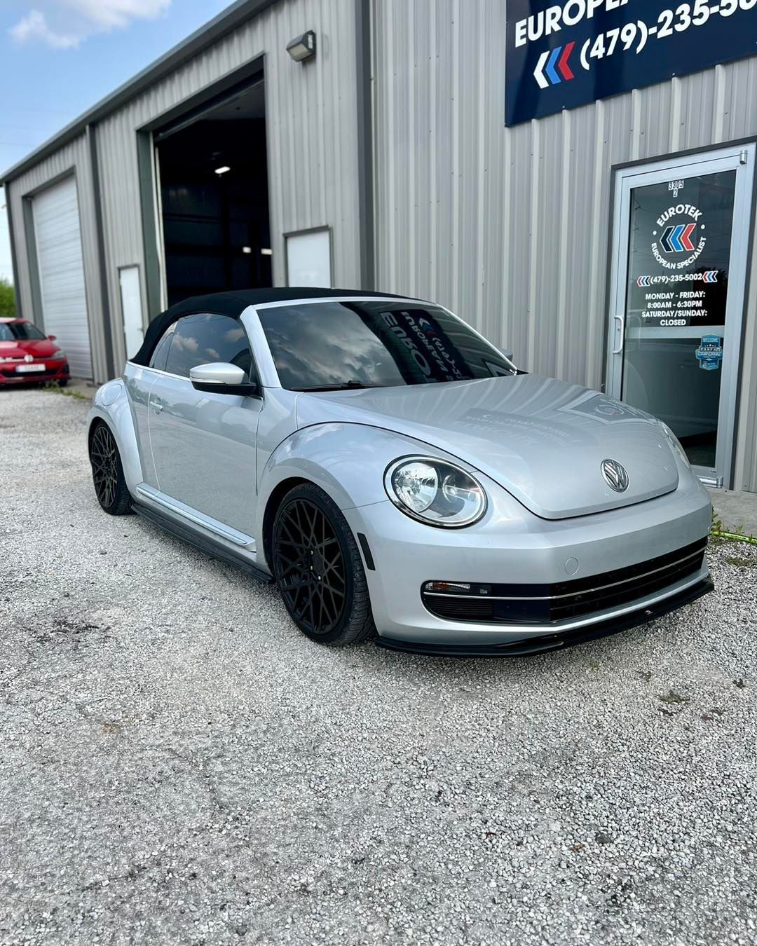 A silver volkswagen beetle convertible is parked in front of a building.