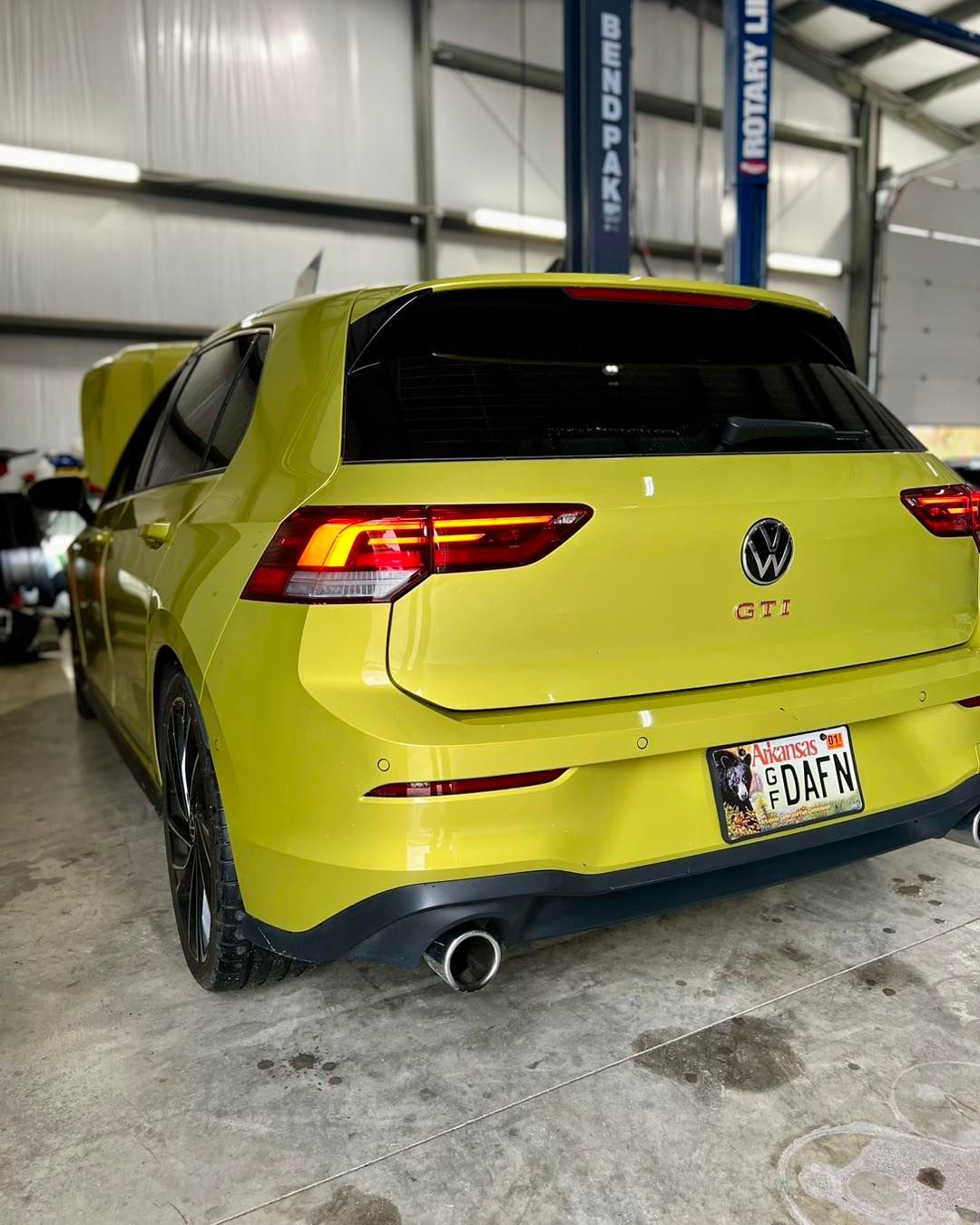 A yellow volkswagen golf is parked in a garage with the hood up.