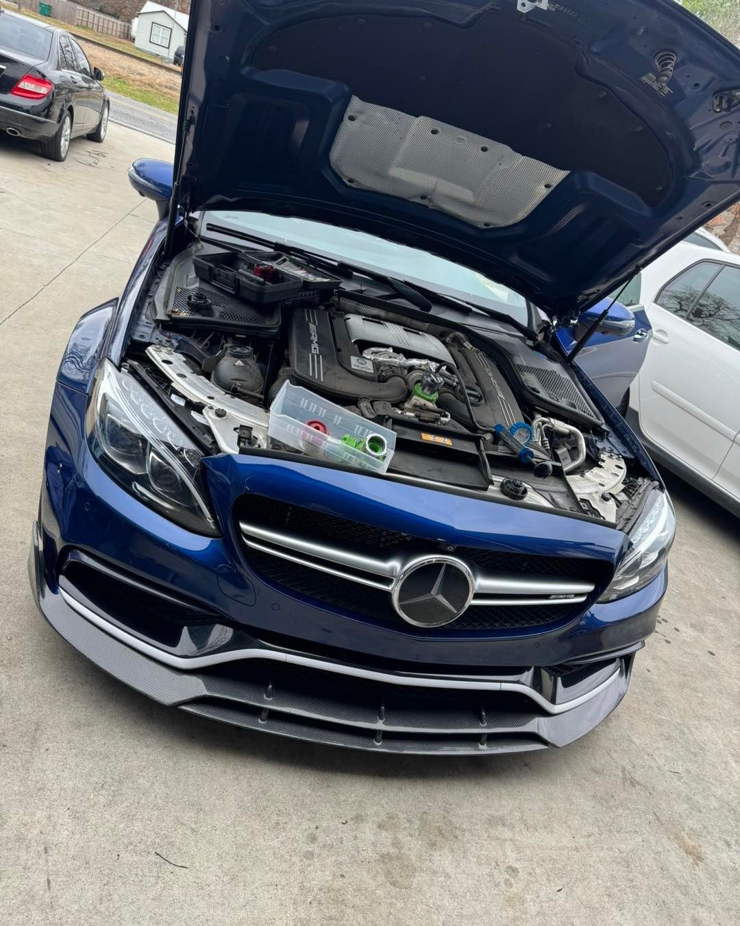 A blue mercedes benz with the hood open is parked in a parking lot.