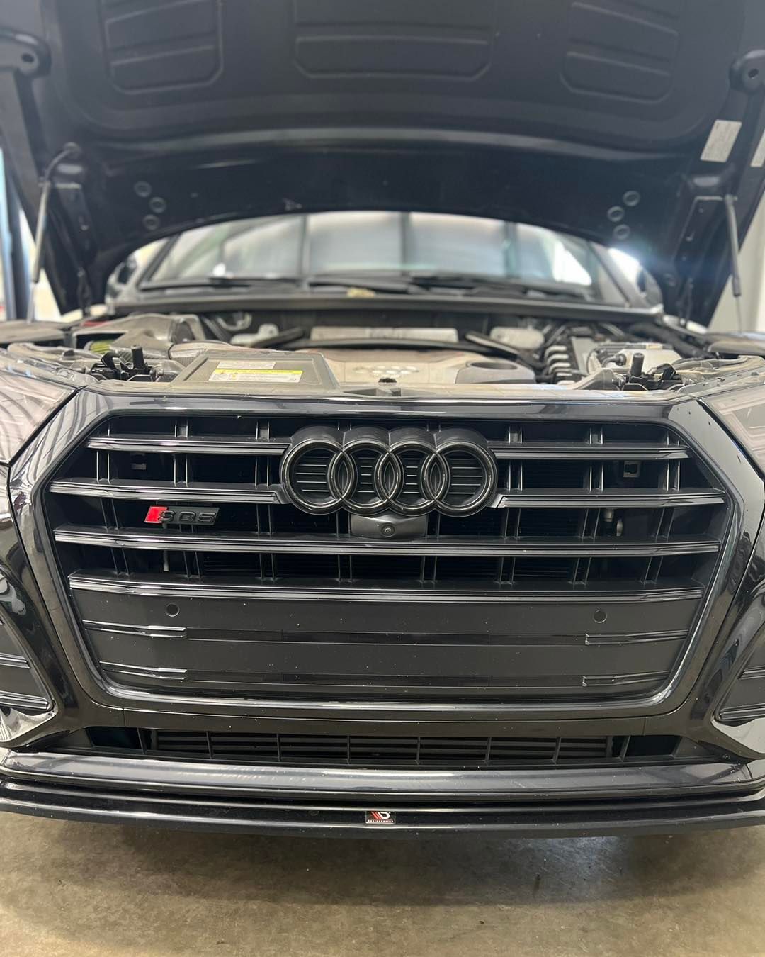 The front of a black audi with the hood open.