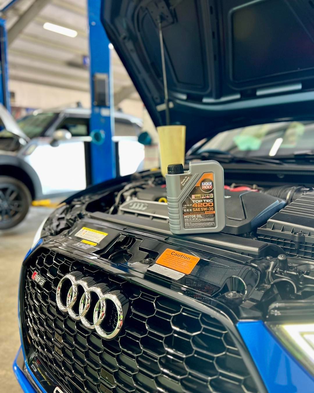 A blue audi with the hood open and a bottle of oil on the hood.