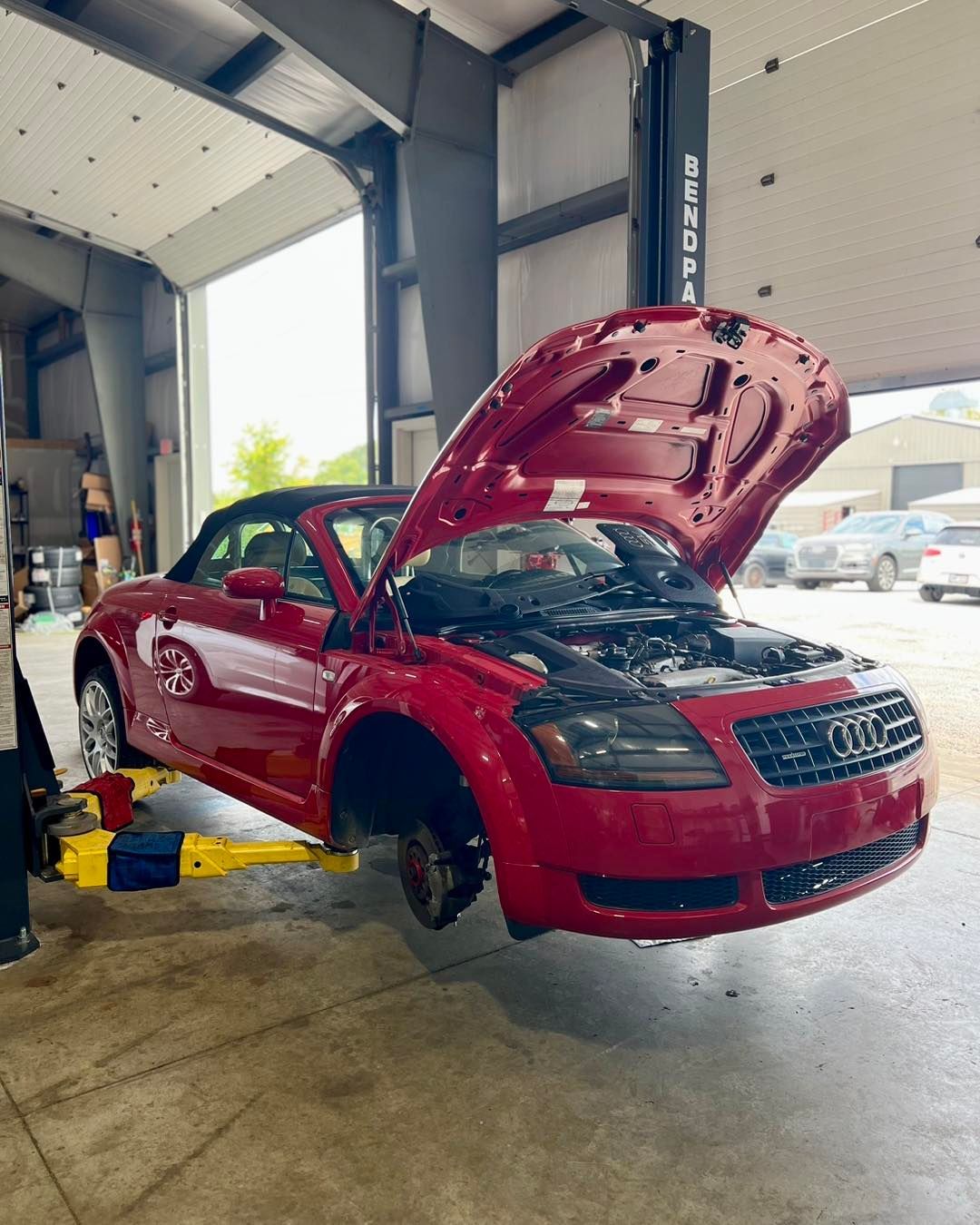 A red audi tt is sitting on a lift in a garage with its hood open.