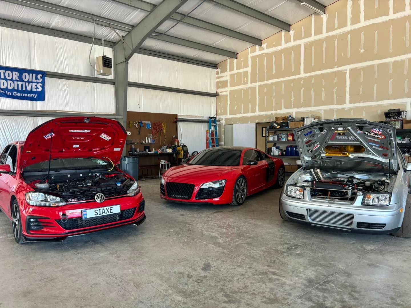 Three cars are parked in a garage with their hoods open.