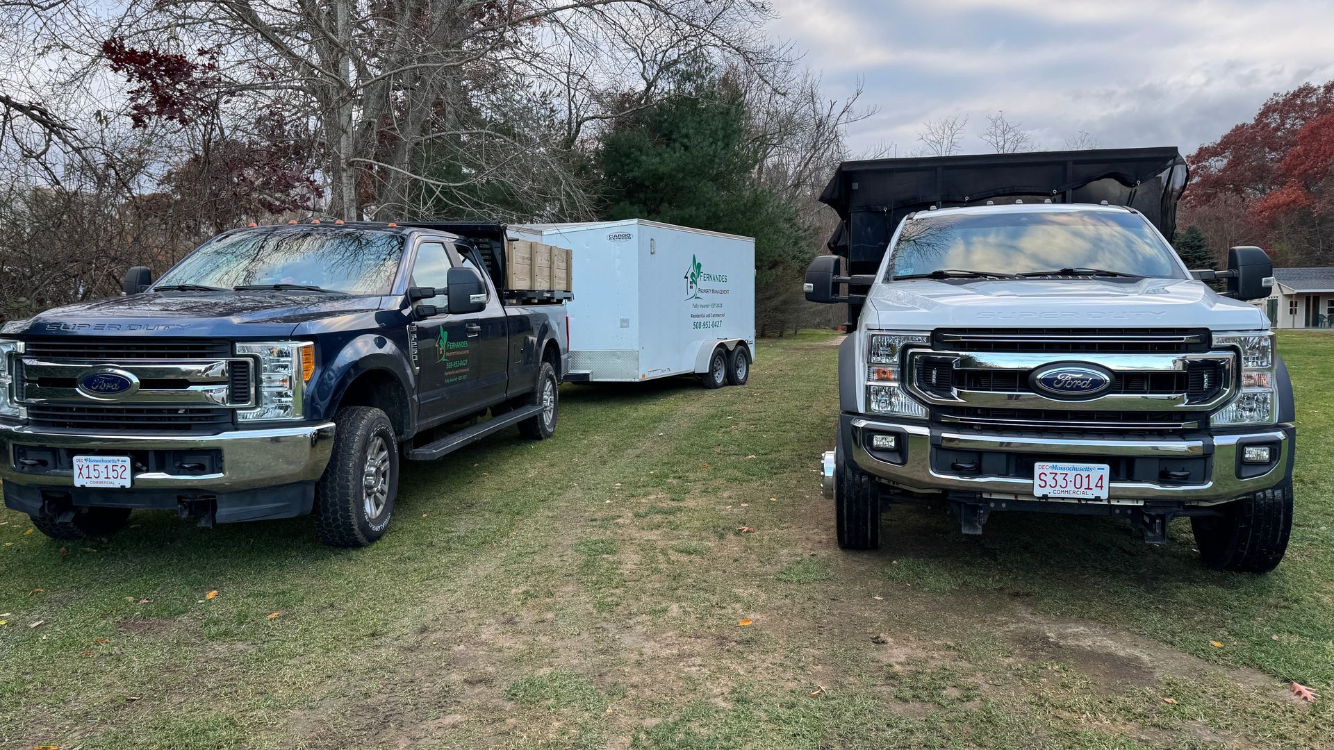 Two Ford trucks parked on grass, one pulling a trailer, and a third vehicle in the background.