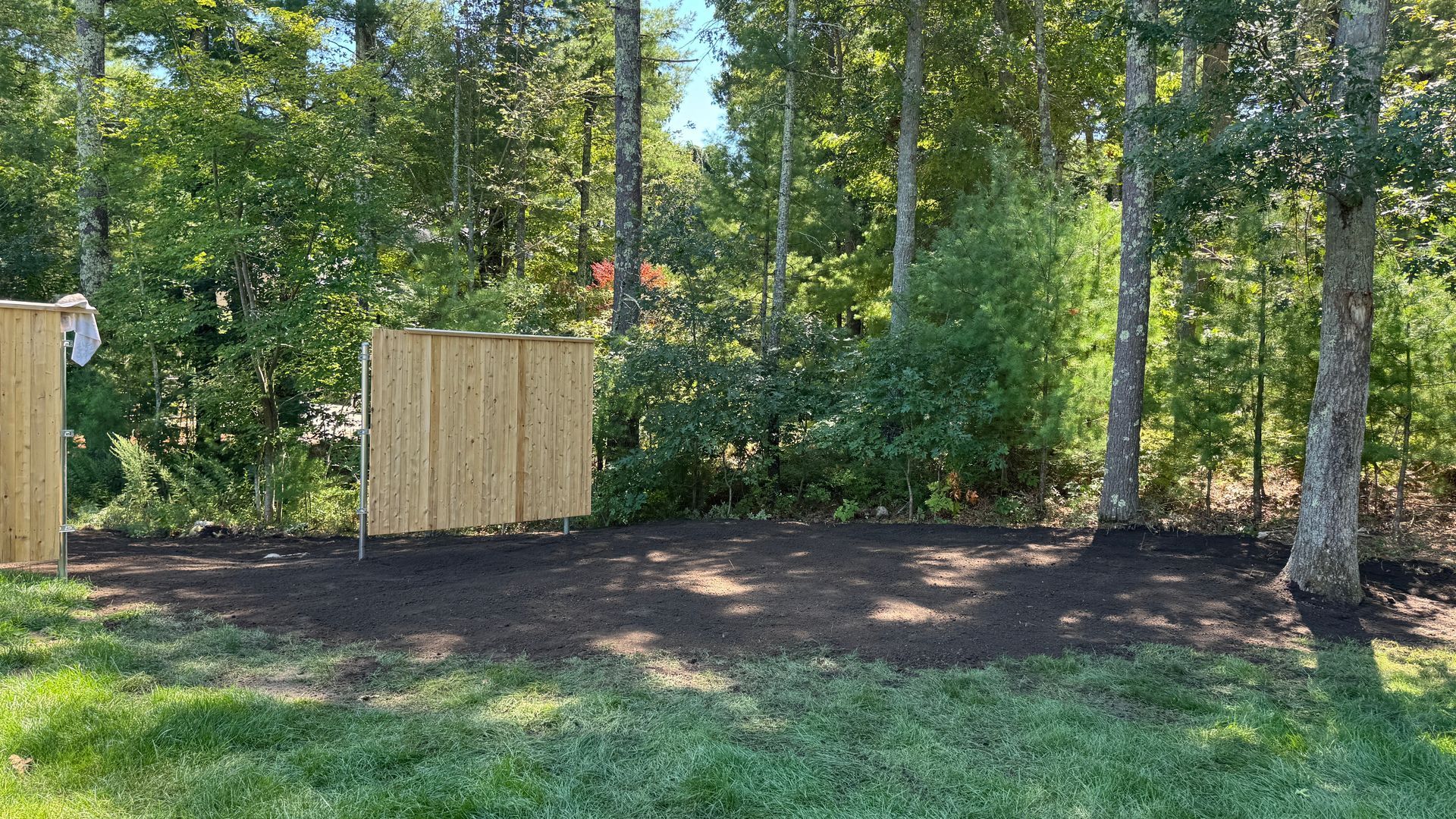 Clearing in backyard, two bamboo privacy screens, fresh mulch, surrounded by trees and green grass.