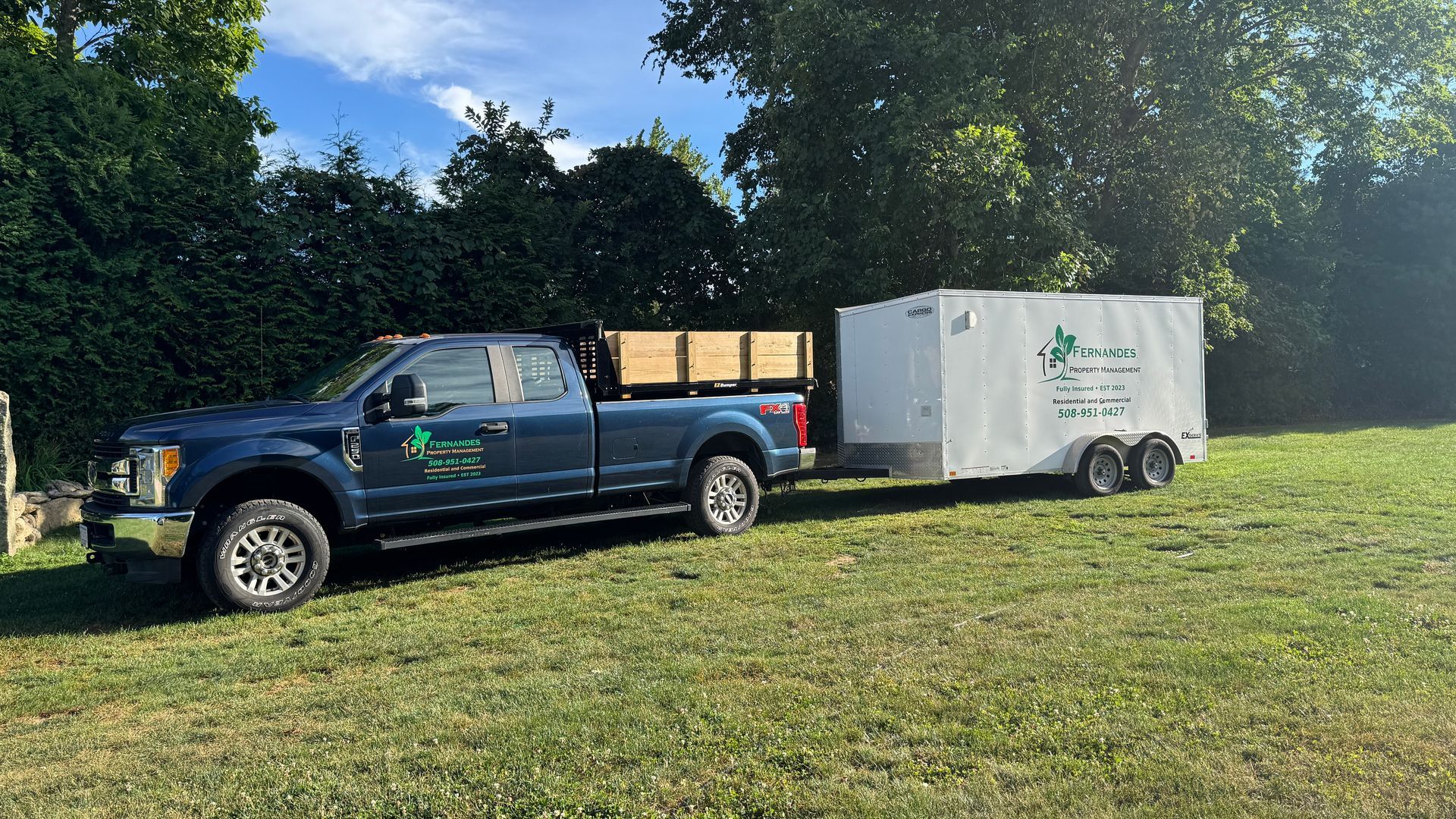 Blue pickup truck with trailer on grass, likely for landscaping services.