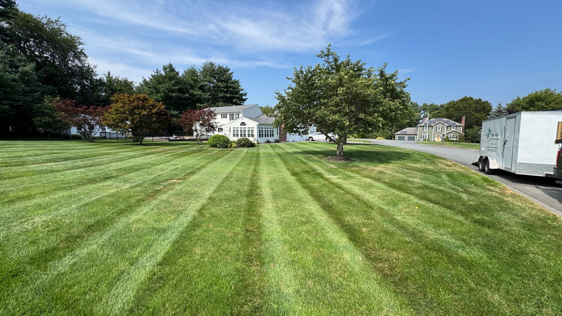 Lawn with freshly cut stripes leads to a white house under a blue sky.
