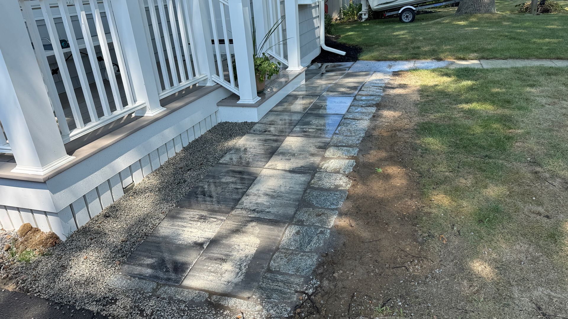 Brick pathway alongside a white porch, leading to a grassy yard.