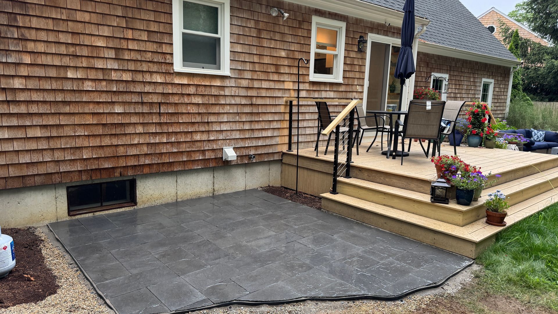 Backyard patio with composite decking, steps, and a black paver patio. Brown house siding, and furniture.