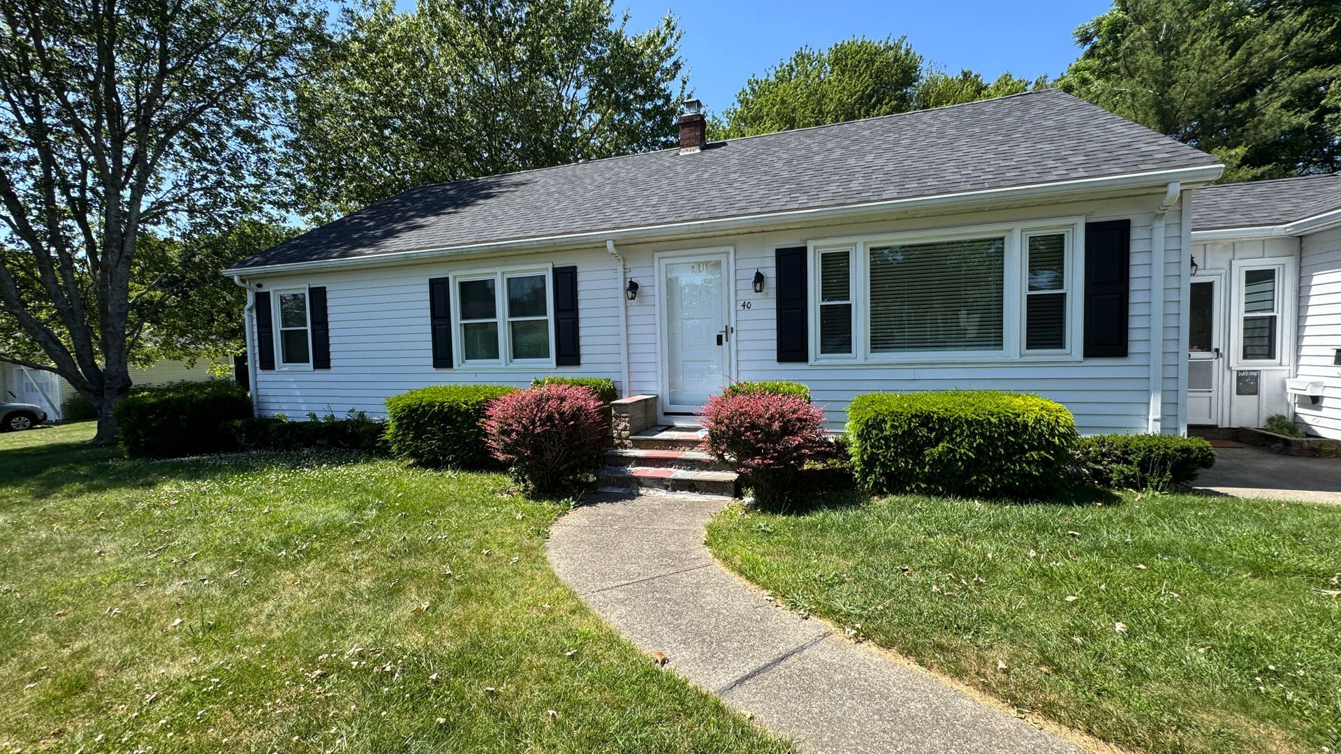 White house with black shutters, walkway, and green lawn.
