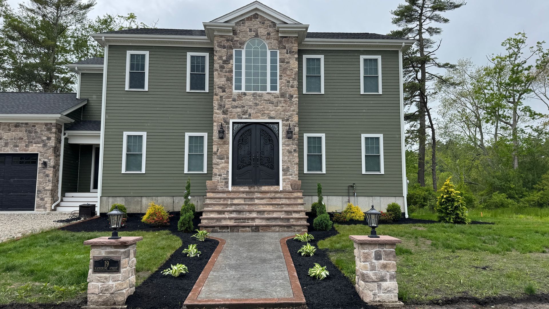 Two-story house with green siding, stone accents, and a dark front door, with a stone path leading to the entrance.