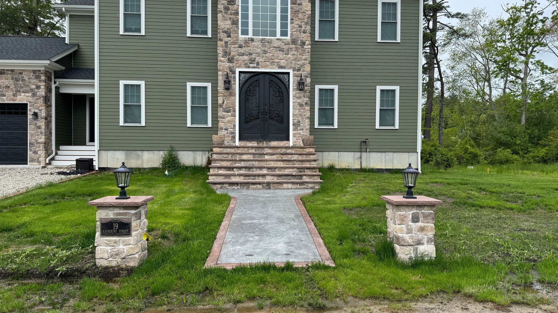 A two-story home with stone accents and a paved walkway leading to the front door, flanked by lamp posts.
