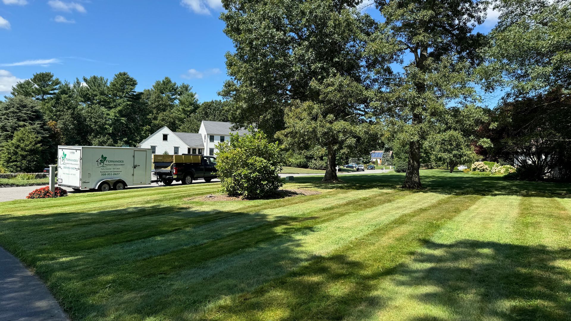 Lawn mowed in stripes; white trailer and truck on a sunny day in front of a house.
