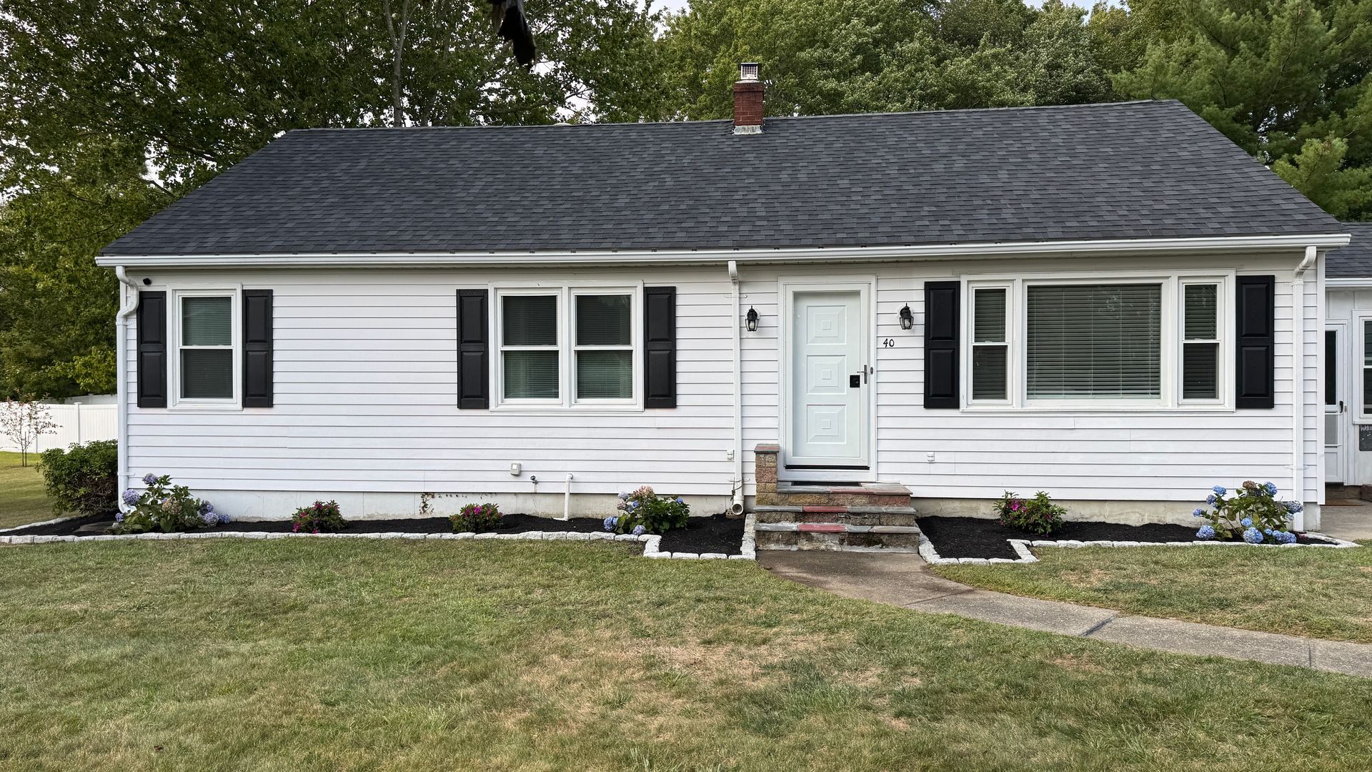 White one-story house with black shutters and roof, small front yard, cloudy sky.