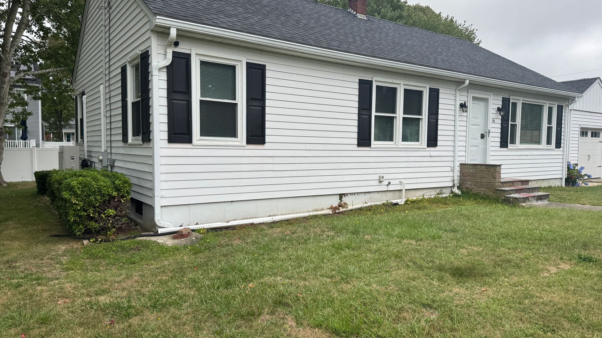White house with black shutters, on a grassy lawn.