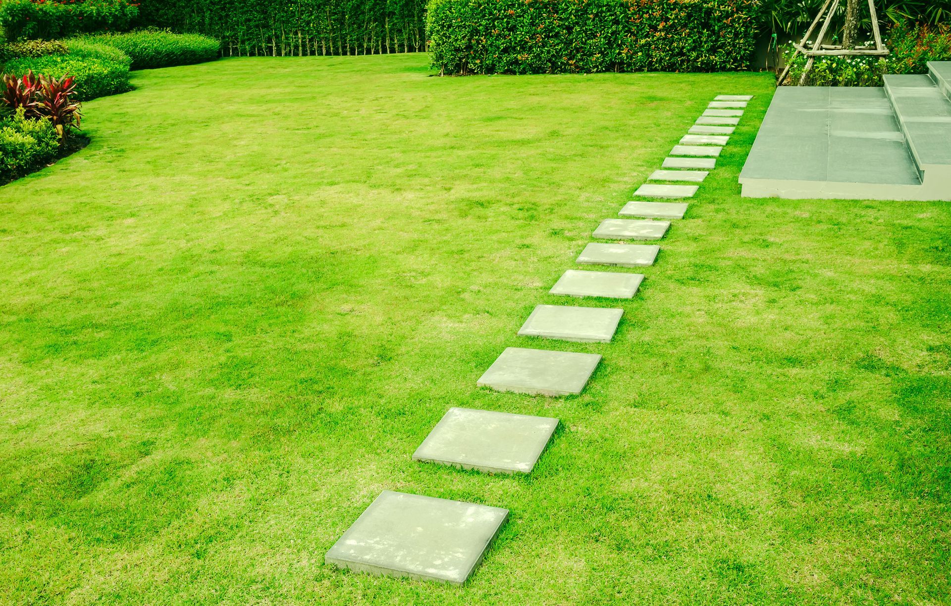 Square stepping stones on green grass leading to an outdoor structure.