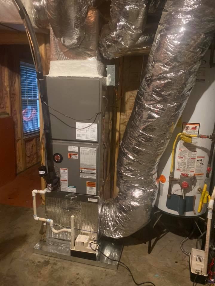 A water heater is sitting next to a heating system in a basement.
