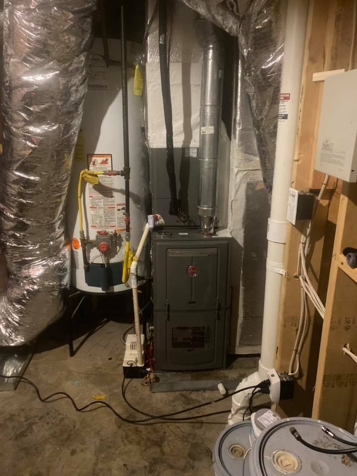 A furnace is sitting in a basement next to a water heater.