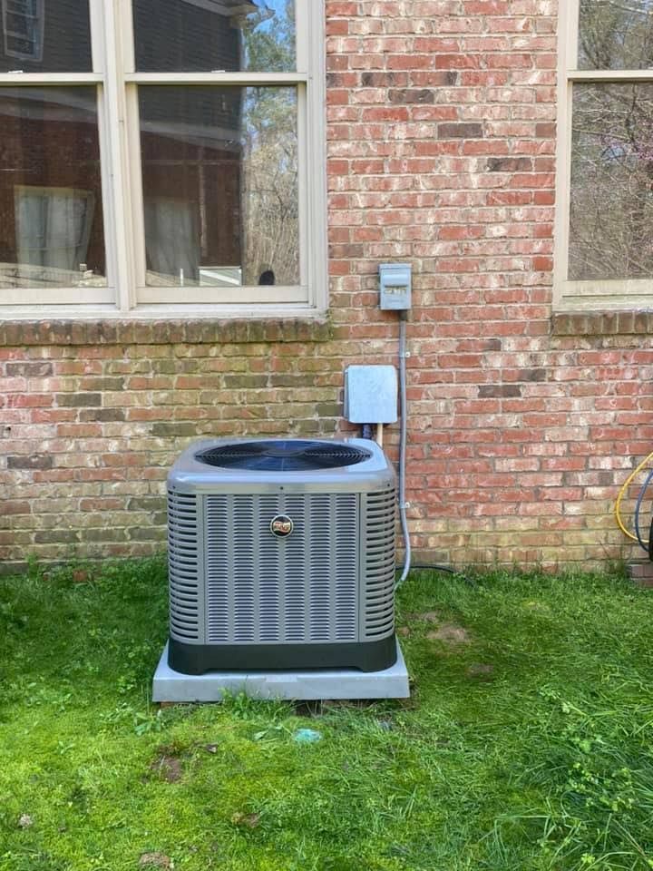An air conditioner is sitting in the grass in front of a brick building.