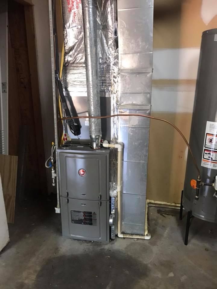 A furnace is sitting in a basement next to a water heater.