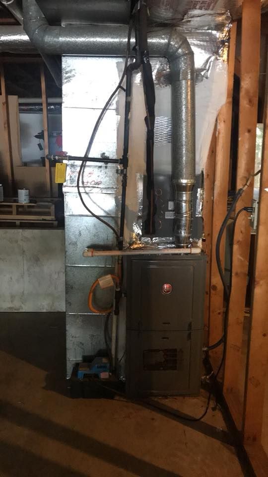 A furnace is sitting in a basement next to a wooden wall.