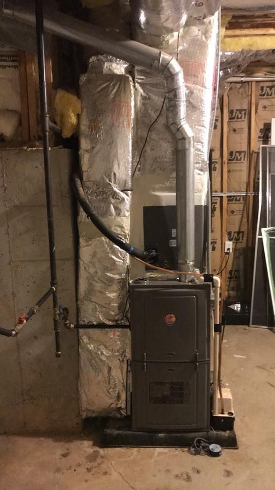 A furnace is sitting in a basement next to a wall.