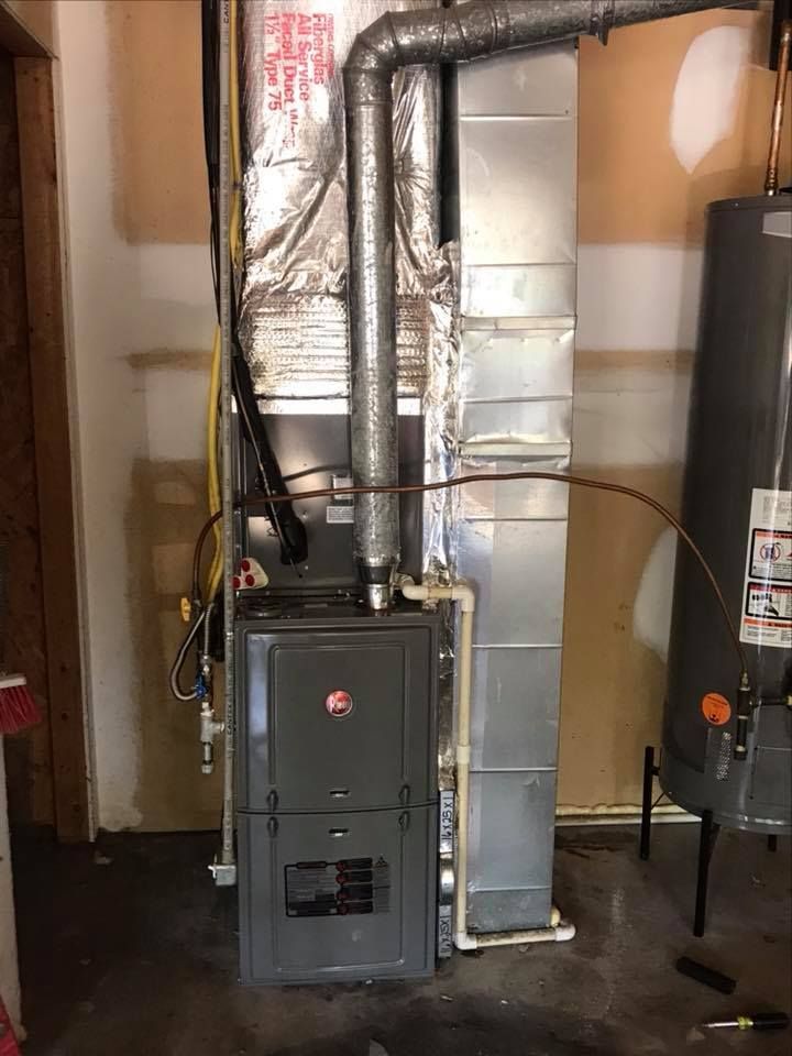 A furnace is sitting in a garage next to a water heater.