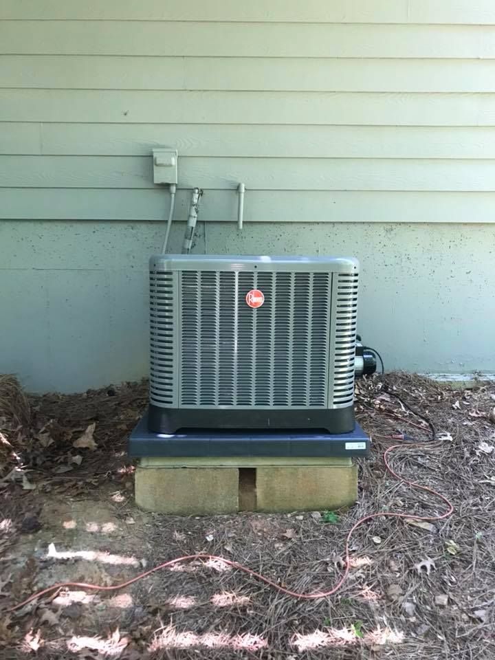 An air conditioner is sitting on top of a concrete block next to a house.