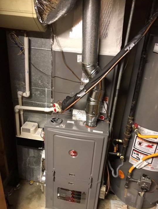 A heater is sitting next to a water heater in a basement.