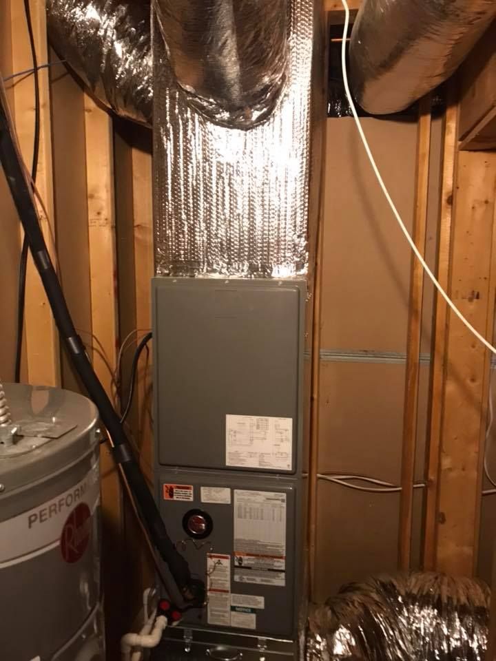 A furnace is sitting in a basement next to a water heater.