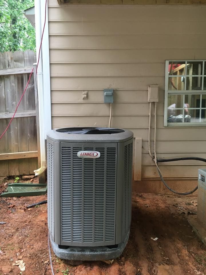 An air conditioner is sitting outside of a house next to a window.