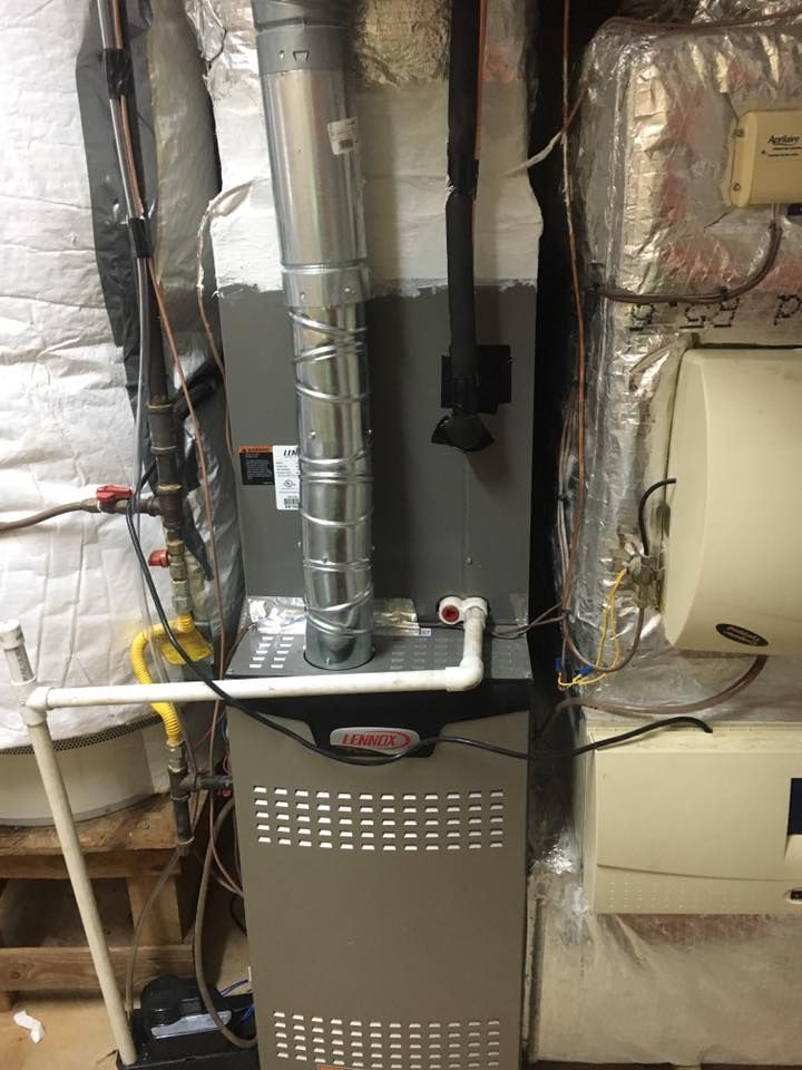 A furnace is sitting in a basement next to a water heater.
