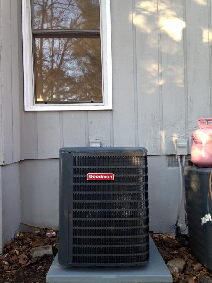 An air conditioner is sitting outside of a house next to a window.