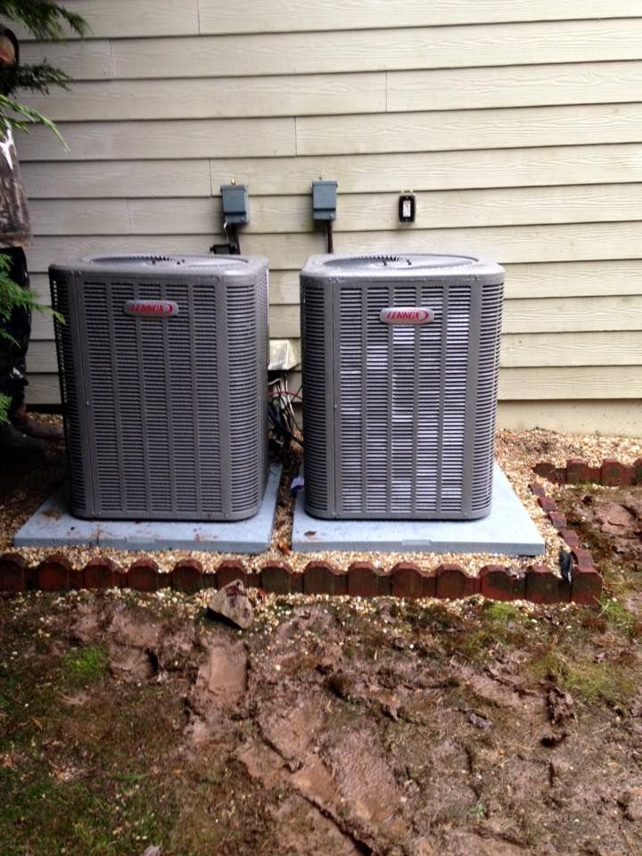 Two air conditioners are sitting next to each other outside of a house.