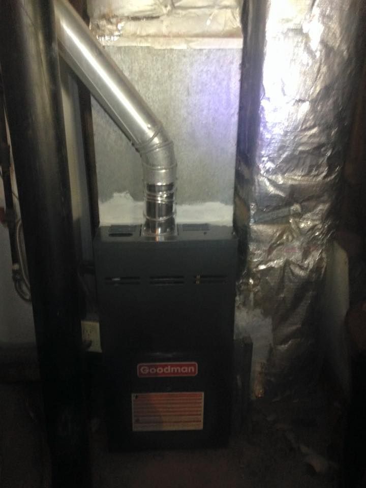 A furnace is sitting in a basement next to a pipe.