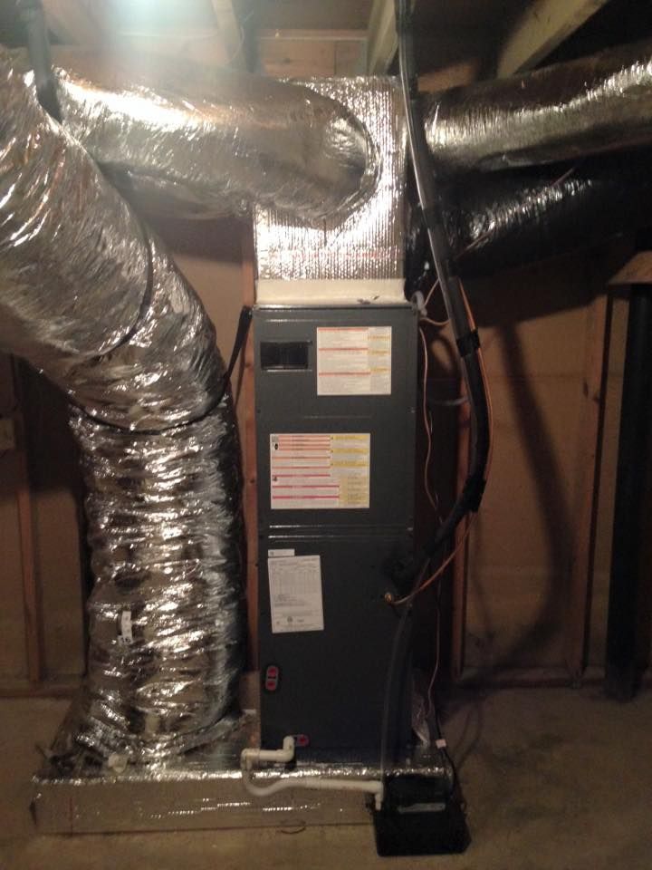 An air conditioner is sitting in a basement next to a bunch of ducts.