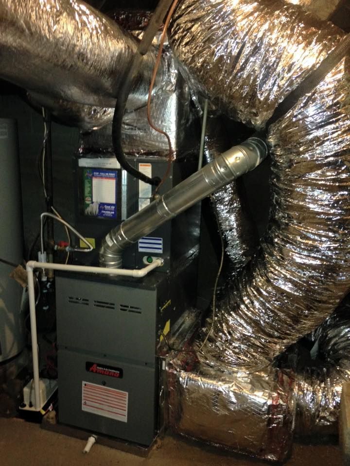 An air conditioner is sitting in a basement next to a bunch of ducts.
