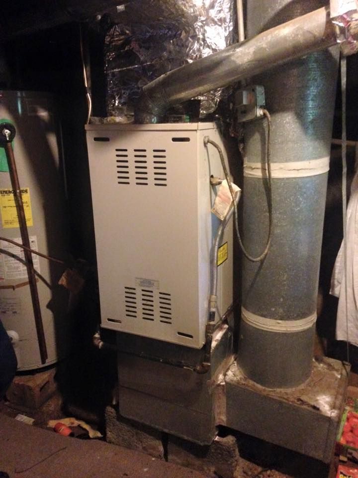 An air conditioner is sitting in a basement next to a water heater.