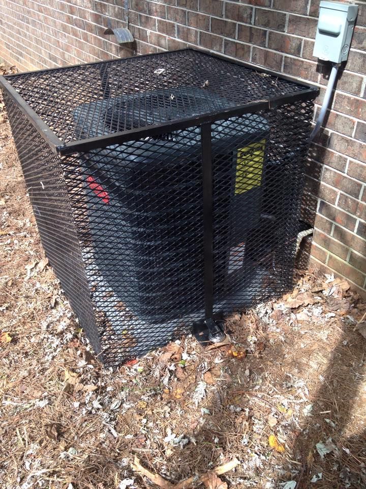 An air conditioner is sitting inside of a metal cage next to a brick wall.