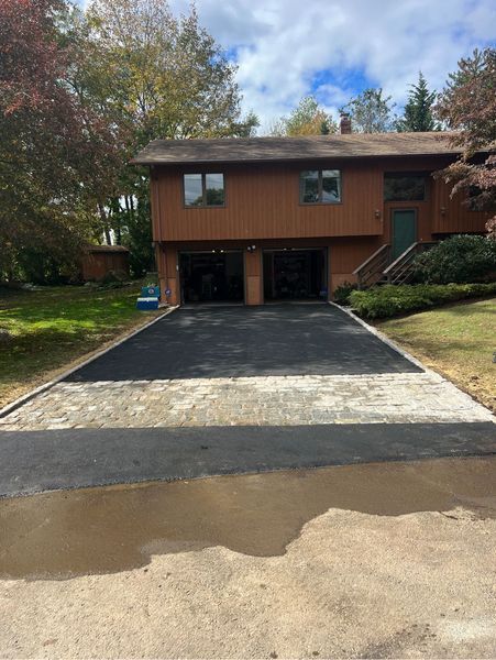 Brown house with open garage doors and newly paved asphalt driveway.