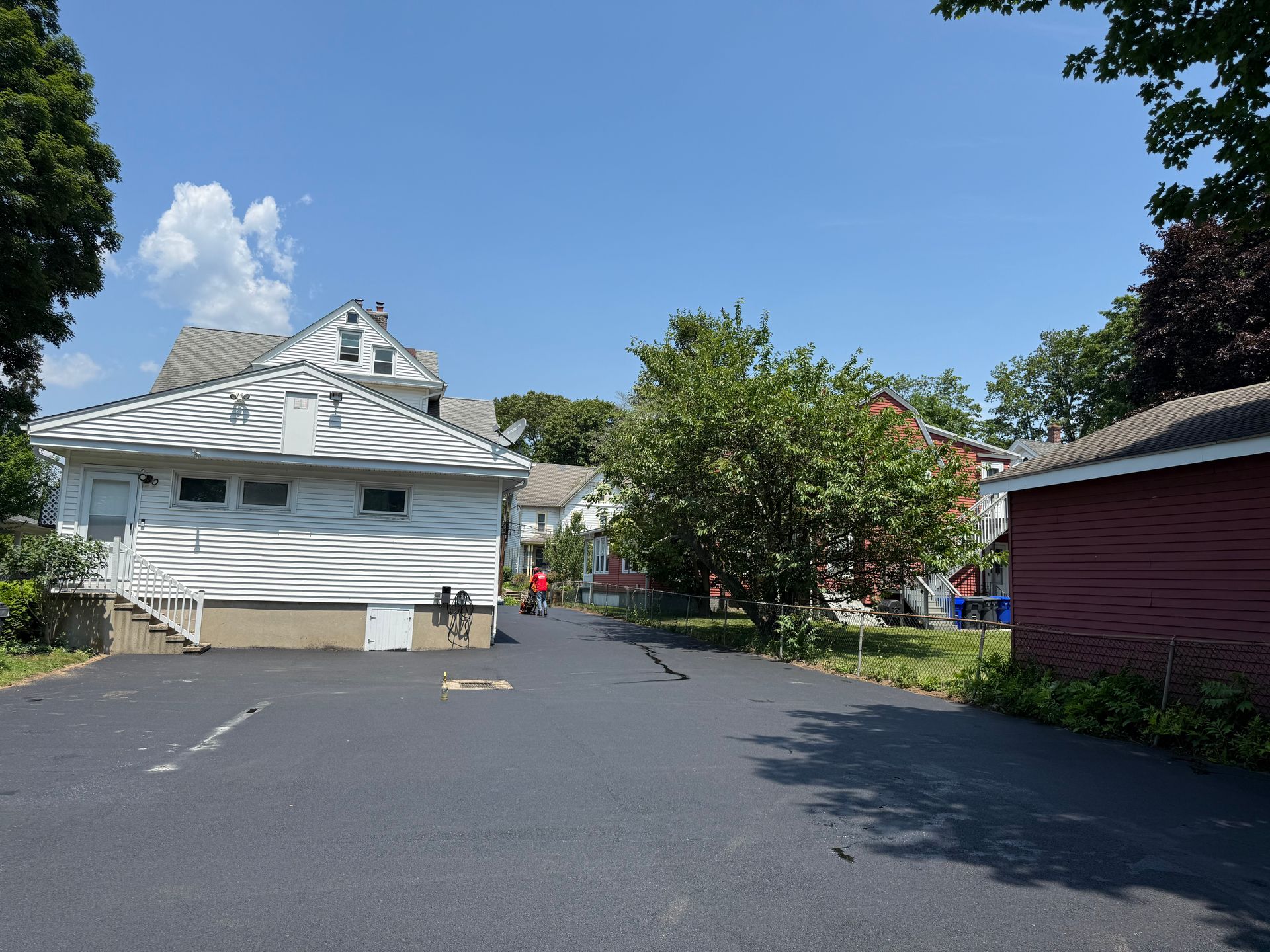 Residential street with houses, trees, and a person walking in the distance on a sunny day.