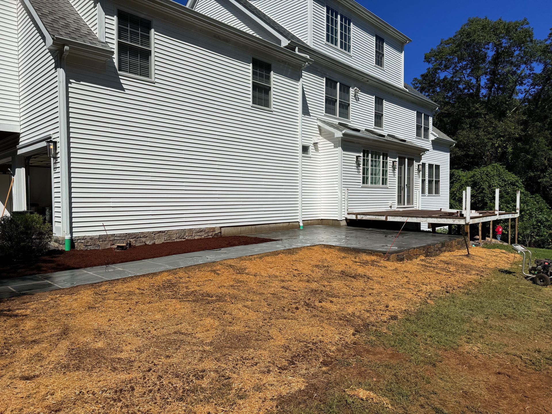 Side view of a white house with siding and a small deck; gravel and mulch landscaping in the yard.