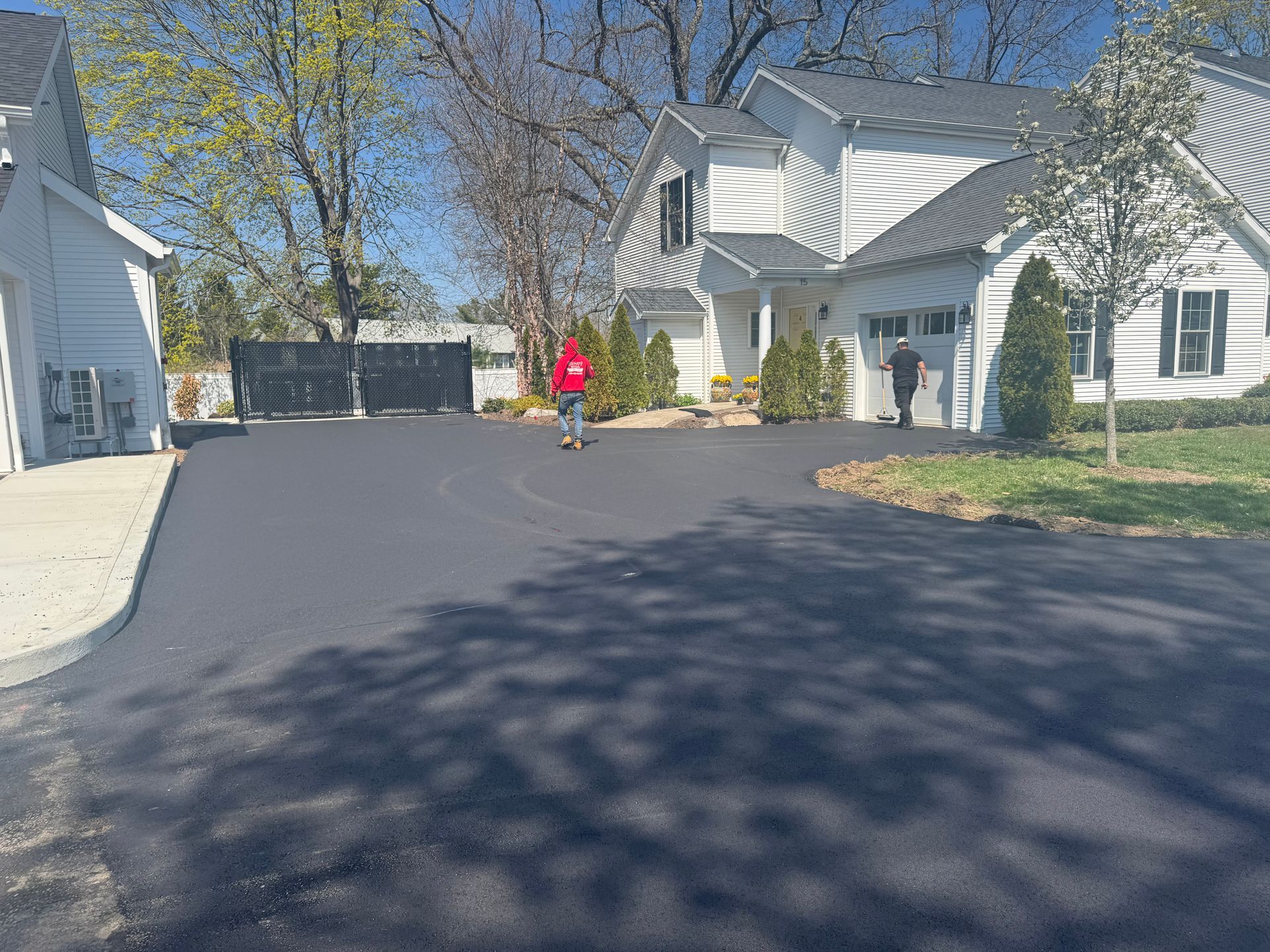 Newly paved asphalt driveway leading to a white house, two people visible.