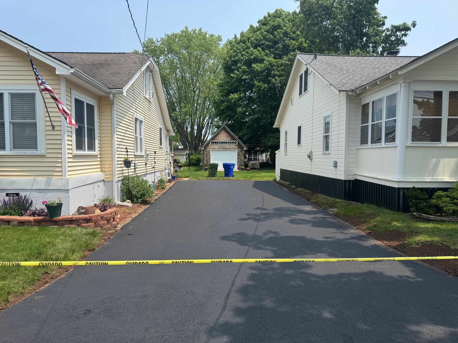 Driveway between two houses, yellow tape across it. Houses are cream and yellow.