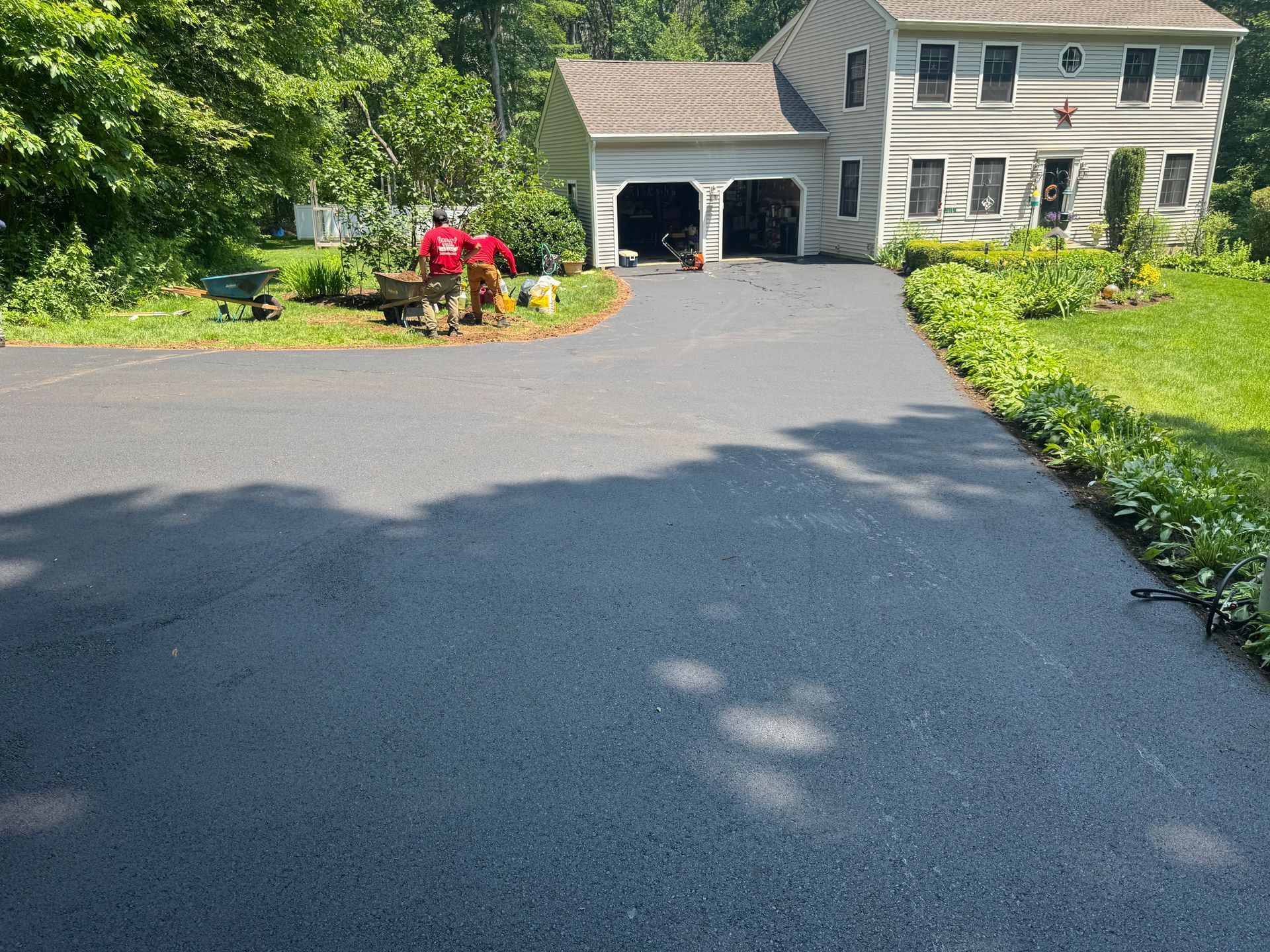 Newly paved asphalt driveway leading to a two-story house with a garage.