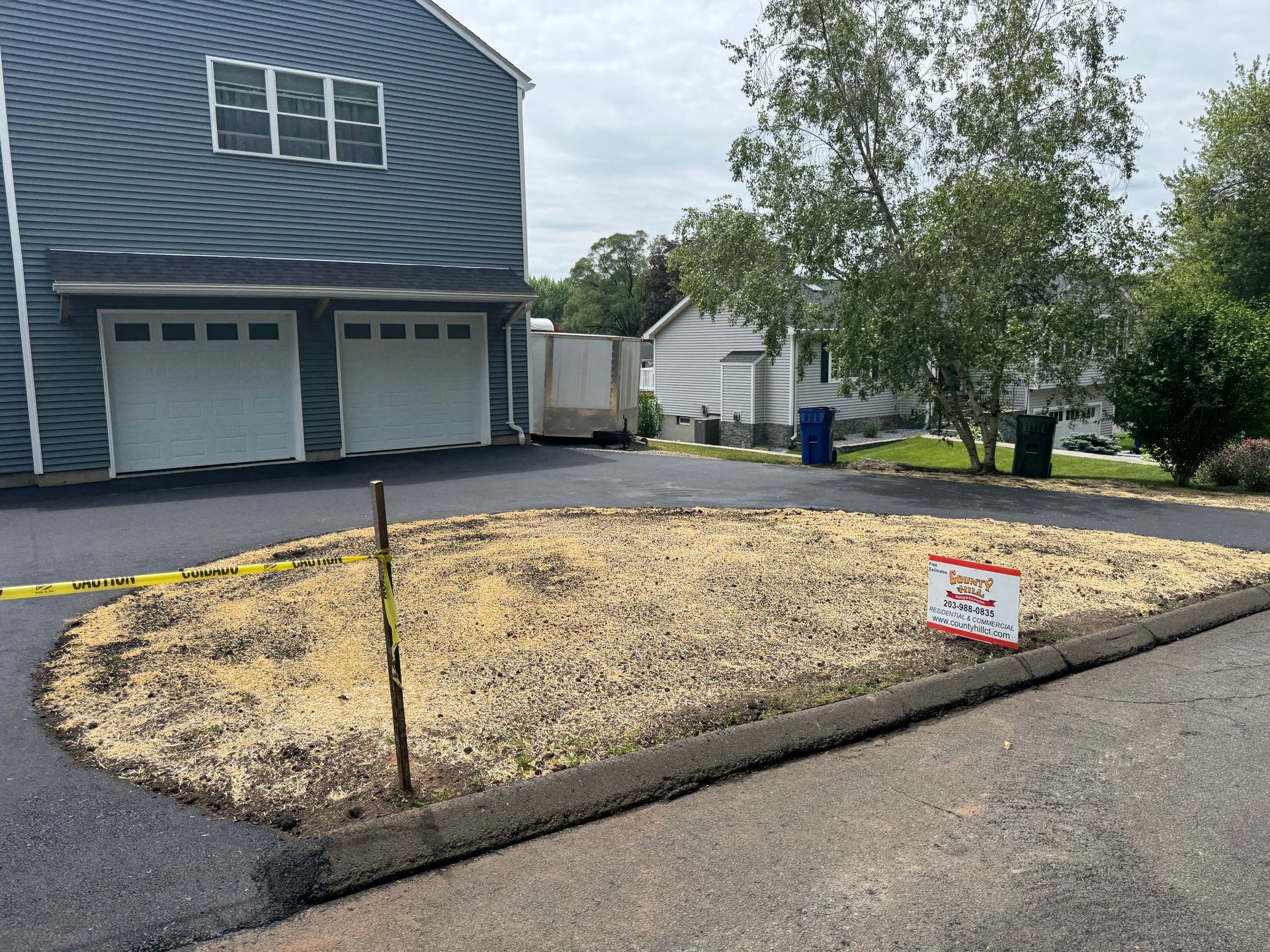 Driveway with a circular patch of mulch; garage in the background, sign on the right.