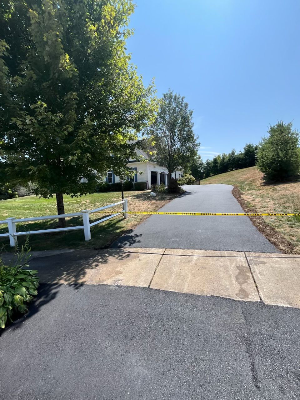 Paved driveway with yellow tape, leading to a white house with a garage, under a bright, sunny sky.