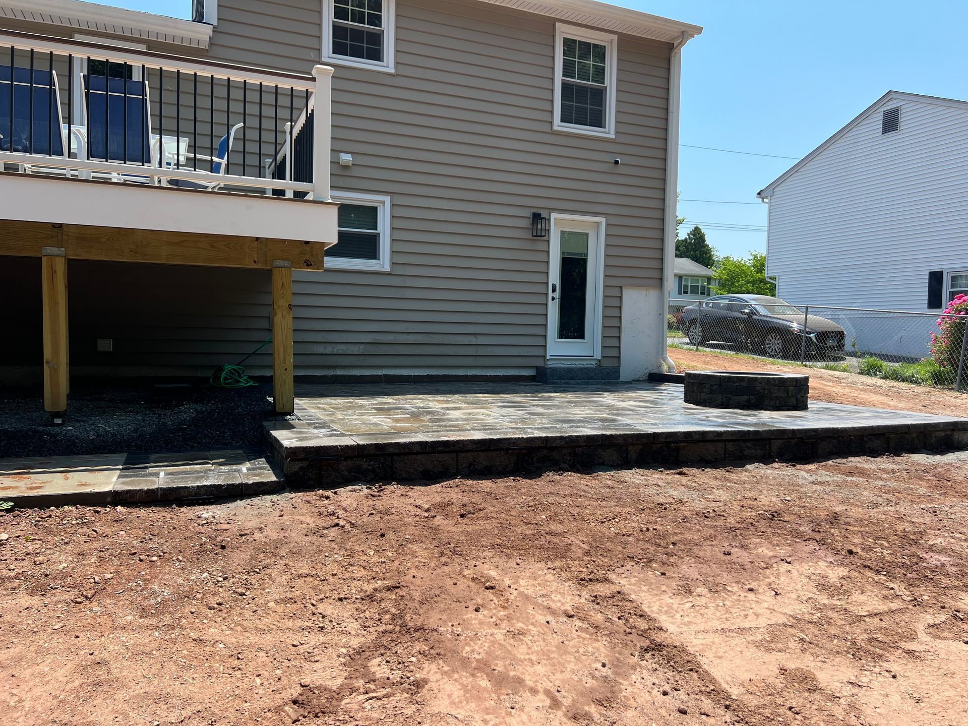 Backyard with new patio, deck, and house with tan siding and windows. Red dirt in foreground.