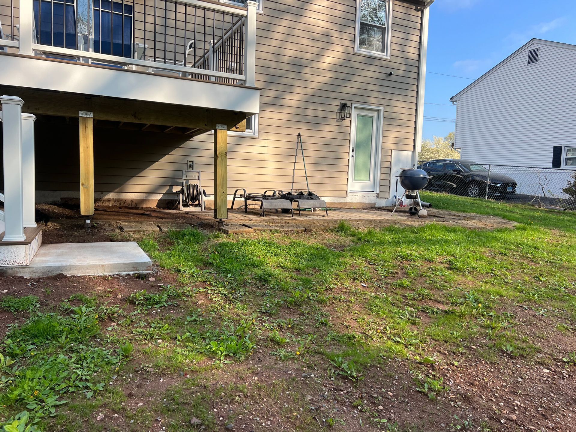 A backyard with a deck and door. Green grass and bare earth in foreground.