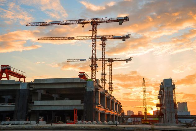 Construction site with cranes and a partially built structure at sunset under a colorful sky